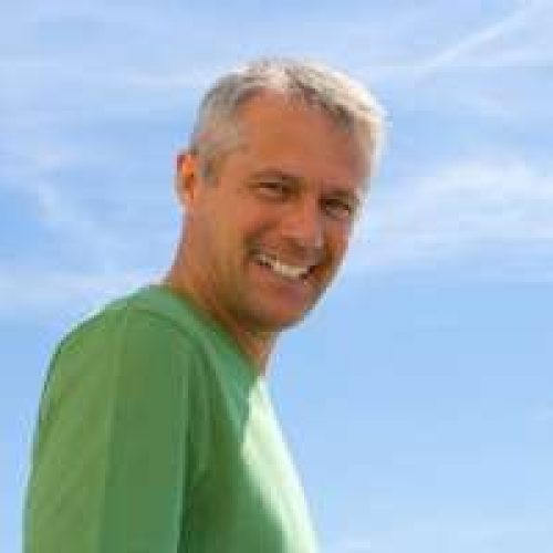 Head and shoulders of a tanned, laughing, fortyish handsome white male wearing green tee-shirt against a blue sky